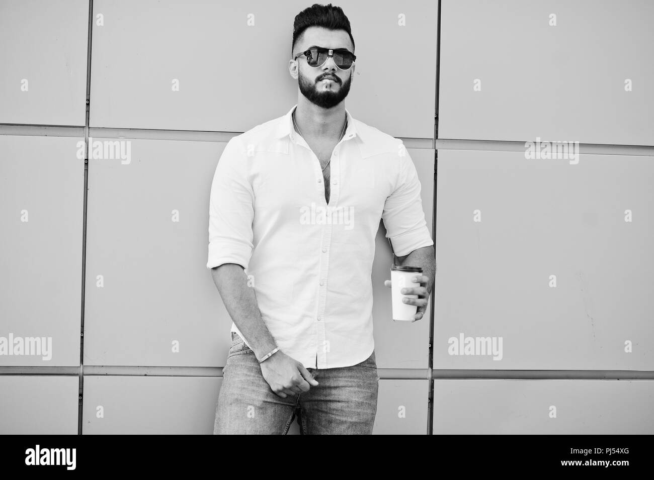 Stylish tall arabian man model in white shirt, jeans and sunglasses posed  at street of city. Beard attractive arab guy with cup of coffee against gold  Stock Photo - Alamy