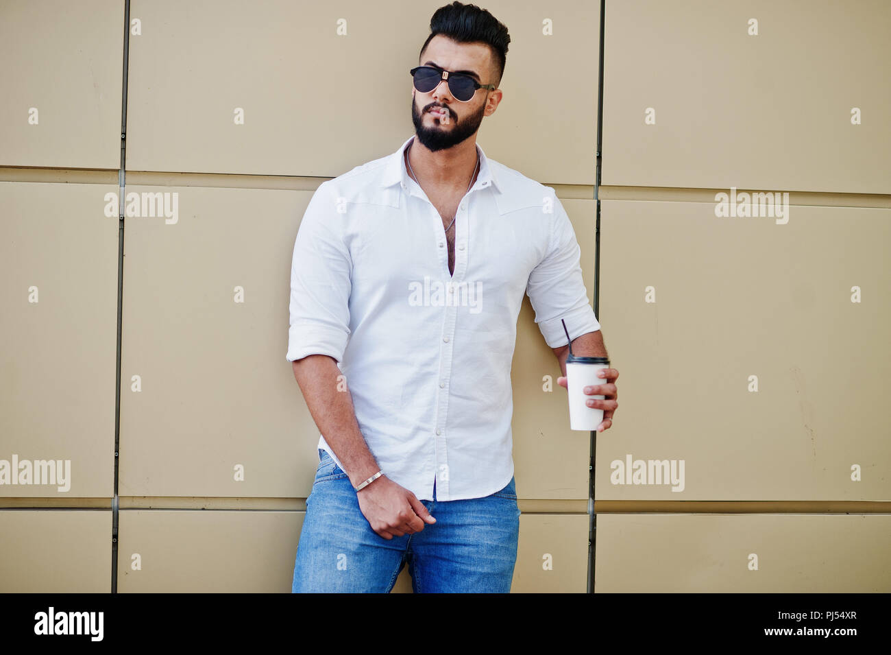 Stylish tall arabian man model in white shirt, jeans and sunglasses posed  at street of city. Beard attractive arab guy with cup of coffee against gold  Stock Photo - Alamy