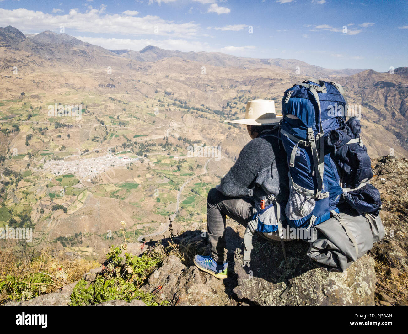 Traveler man with hat and backpack sitting on a rock watching the landscape, Travel lifestyle Stock Photo