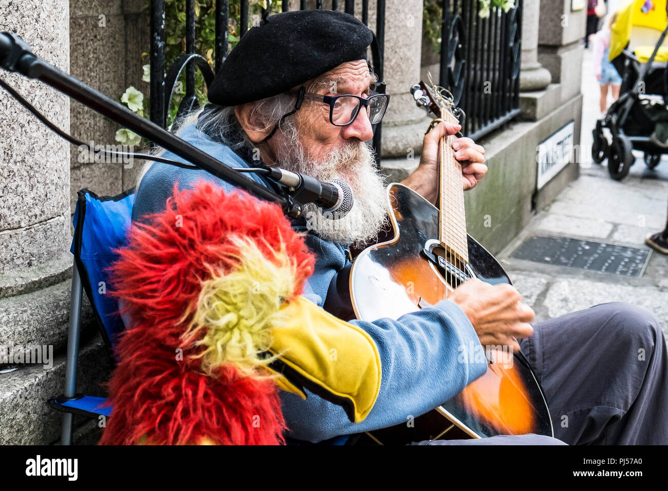 A mature busker playing the guitar and singing in a street in Truro Cornwall. Stock Photo
