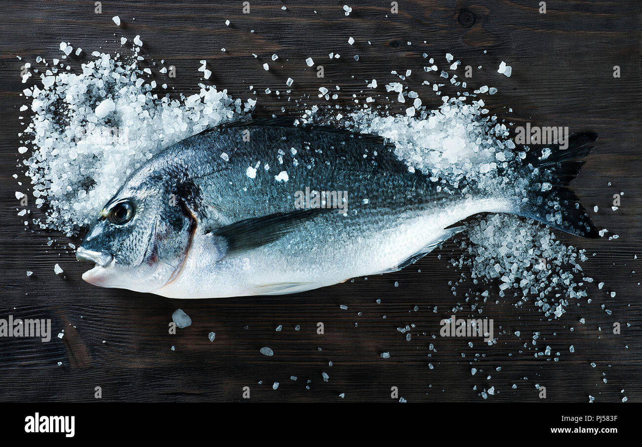 Fresh fish dorado sea bream on black board with salt for cooking magazines and recipes Stock Photo