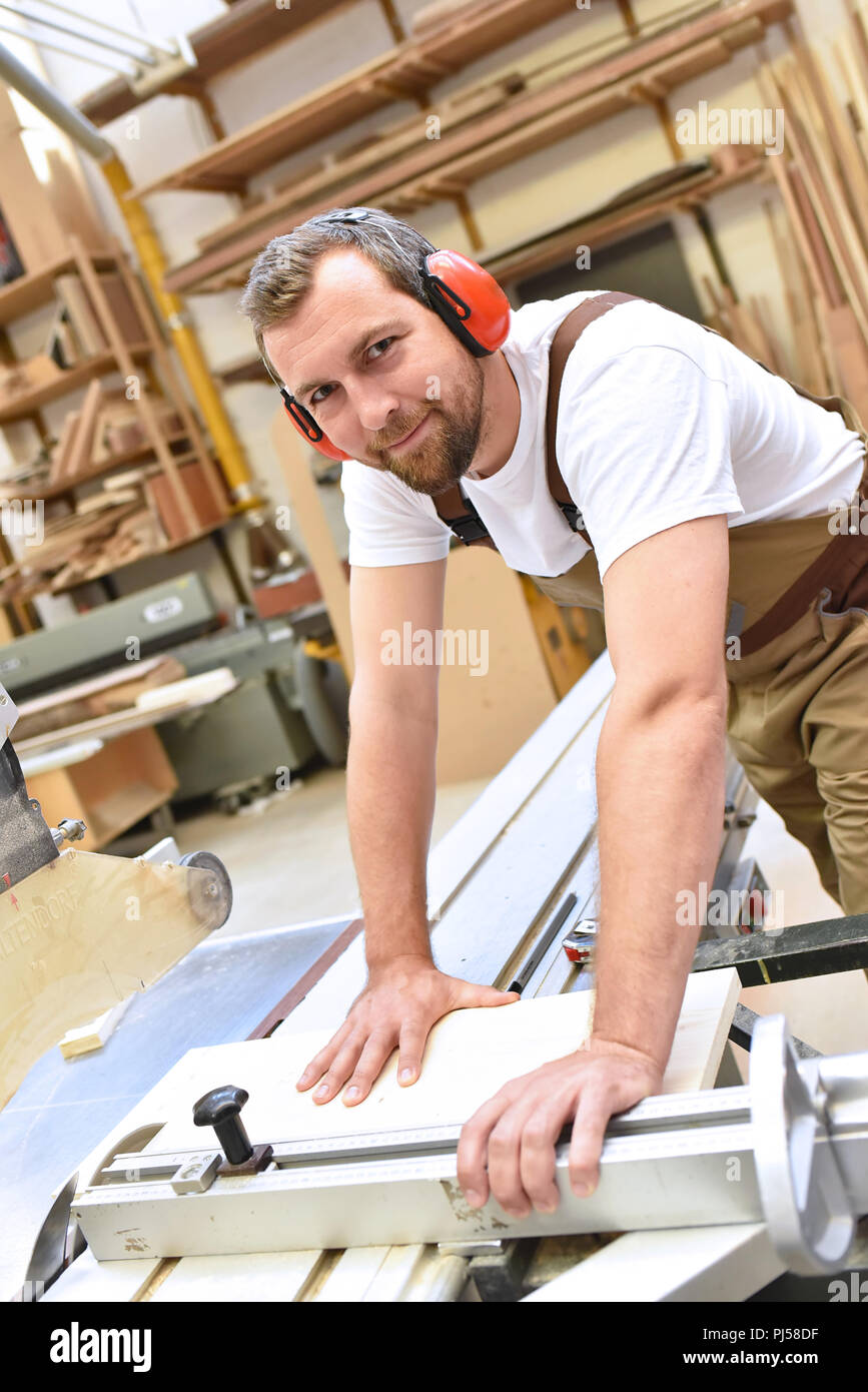 portrait of a carpenter in work clothes and hearing protection in the workshop of a carpenter's shop Stock Photo