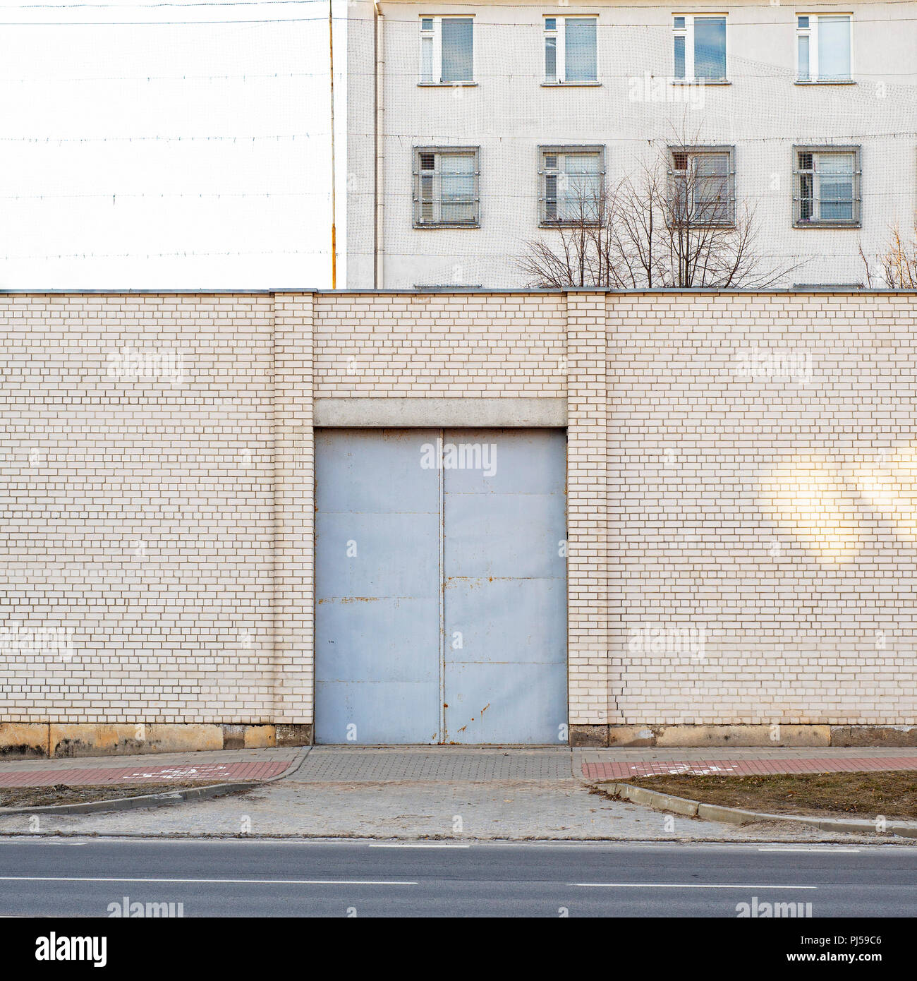 Entrance to abandoned building surrounded by big white brick wall. Industrial background. Stock Photo