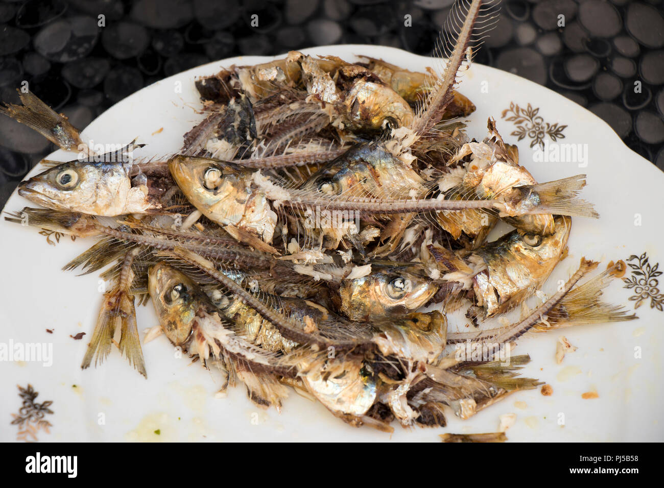 Dozen of home prepared eaten grilled sardines heads and bones on a plate, very healthy, tasty and cheap Mediterranean fish , a rich meal for the poor Stock Photo