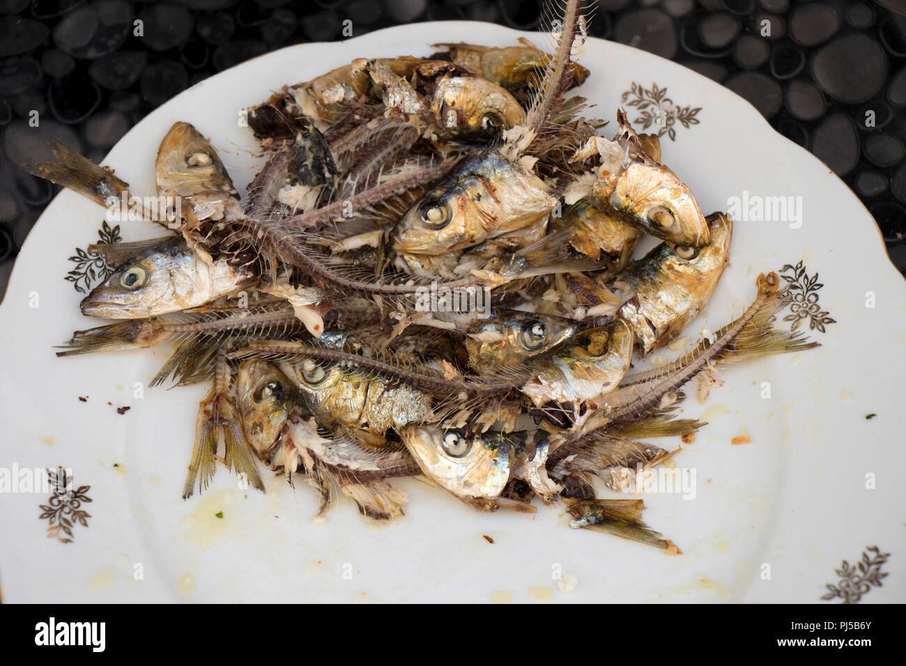 Dozen of home prepared eaten grilled sardines heads and bones, very healthy, tasty and cheap Mediterranean fish , a rich meal for the poor Stock Photo