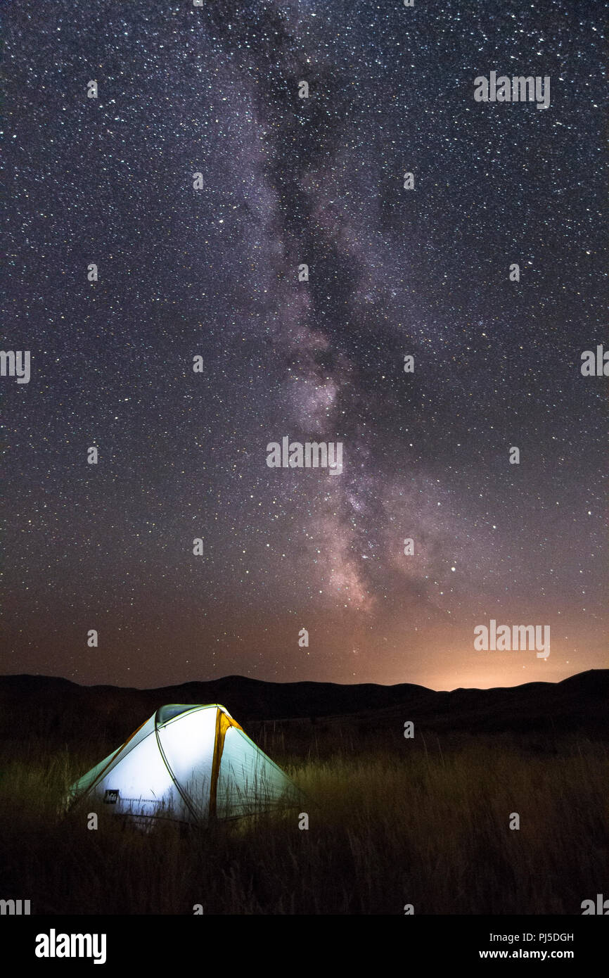 A lit-up tent sits below the Milky Way Galaxy on a starry night in ...