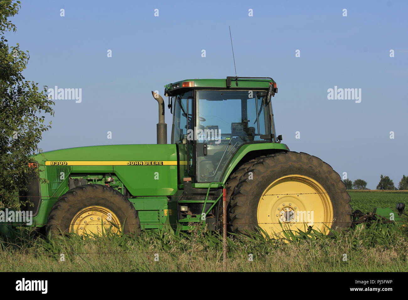 Green John Deere Tractor in a Field with a fence and blue sky. Stock Photo