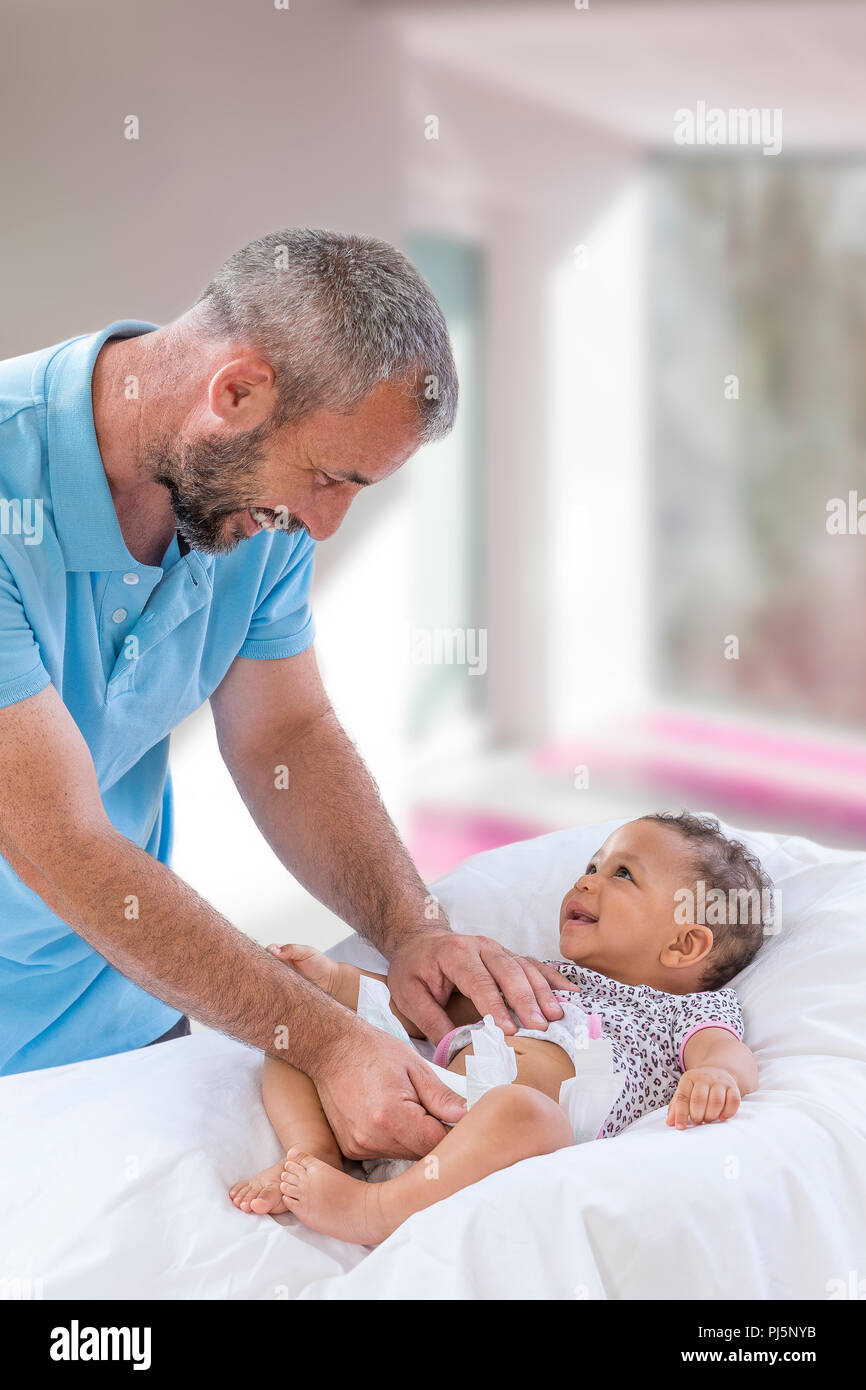 Baby Changing. Loving father changing diaper of his baby daughter.,Little child, girl on changing table in bathroom with rattle toys. Happy dad. Stock Photo
