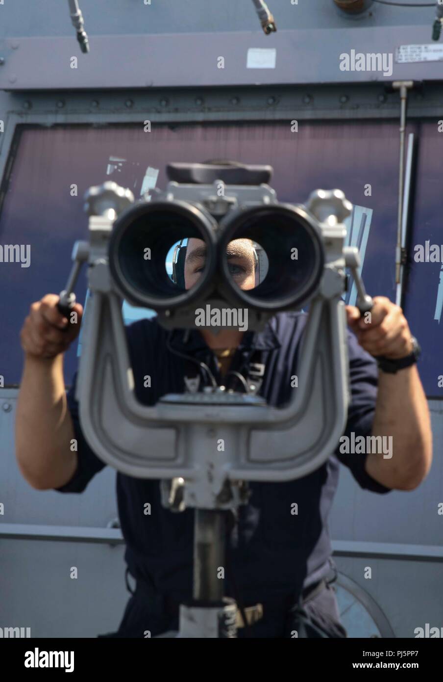 180825-N-HG389-0026 ATLANTIC OCEAN (Aug. 25, 2018) Seaman Andrew Pierce looks through the “big eyes” binoculars on the bridge wing of amphibious transport dock ship USS Arlington (LPD 24) during a visit, board, search and seizure (VBSS) exercise during the Carrier Strike Group FOUR (CSG 4) Amphibious Ready Group, Marine Expeditionary Unit exercise (ARGMEUEX).  Kearsarge Amphibious Ready Group and 22nd Marine Expeditionary Unit are enhancing joint integration, lethality and collective capabilities of the Navy-Marine Corps team through joint planning and execution of challenging and realistic tr Stock Photo
