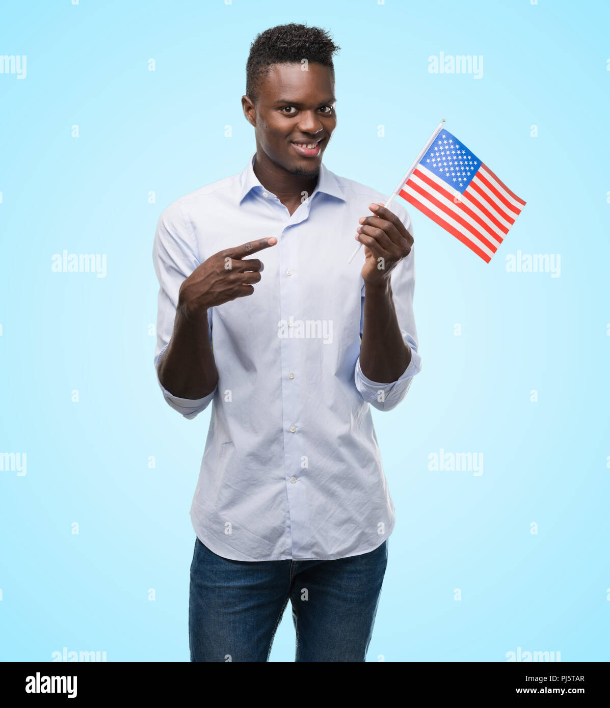 Young african american man holding USA flag very happy pointing with ...