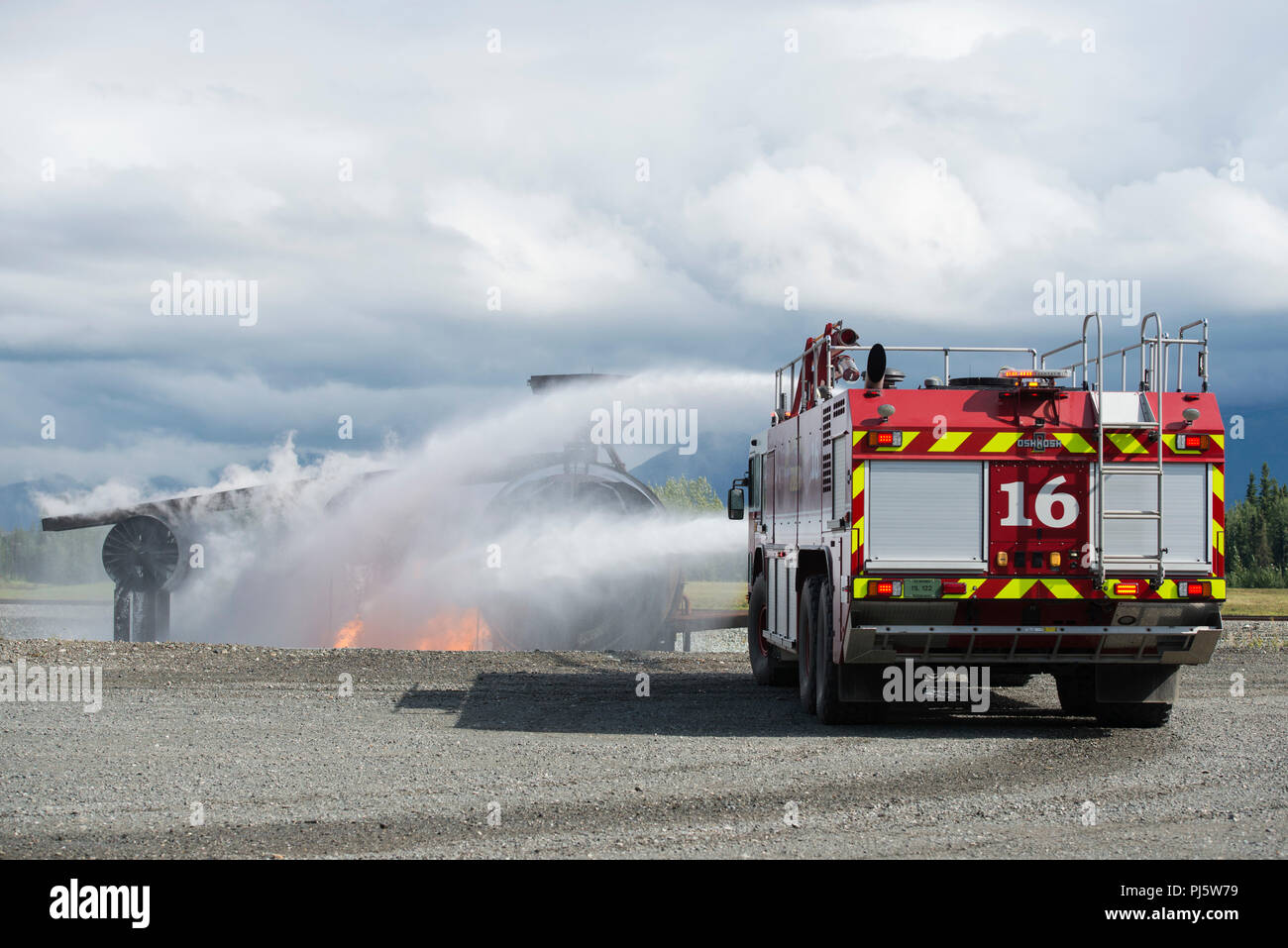 U.S. Air Force fire protection specialists assigned to the 673d Civil Engineer Squadron, spray water from their Striker aircraft rescue and firefighting vehicle while responding to a simulated aircraft fire during wartime-firefighting readiness training at Joint Base Elmendorf-Richardson, Alaska, Aug. 24, 2018. During the readiness training the Air Force firefighters donned various levels of mission oriented protective posture (MOPP) gear and practiced responding to emergency situations in a simulated toxic environment during a chemical, biological, radiological, or nuclear strike. (U.S. Air F Stock Photo