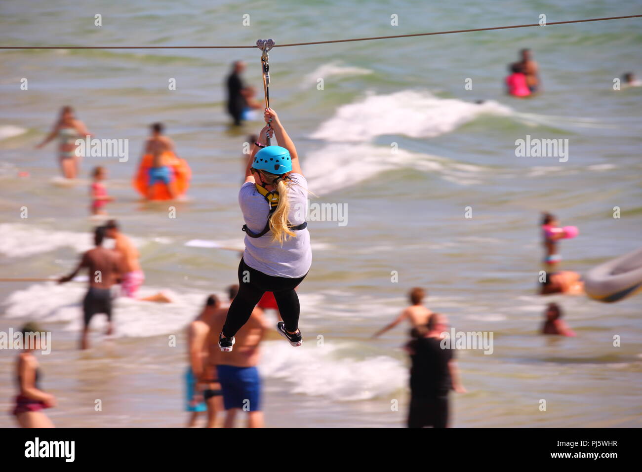 A woman in a harness travels along a zip wire on the beach at Bournemouth, UK Stock Photo