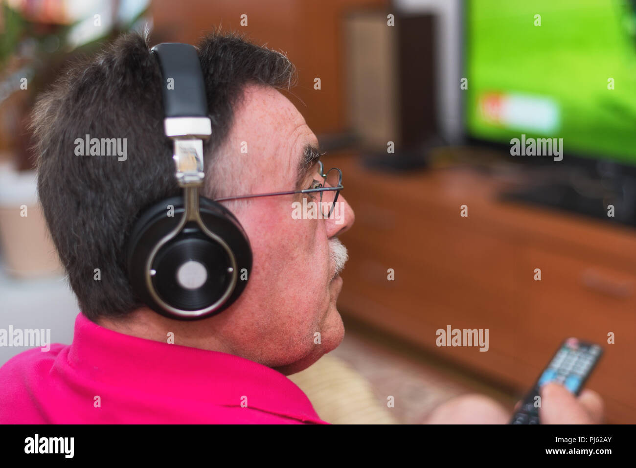 Back view of senior man with headphones watching tv holding remote control Stock Photo
