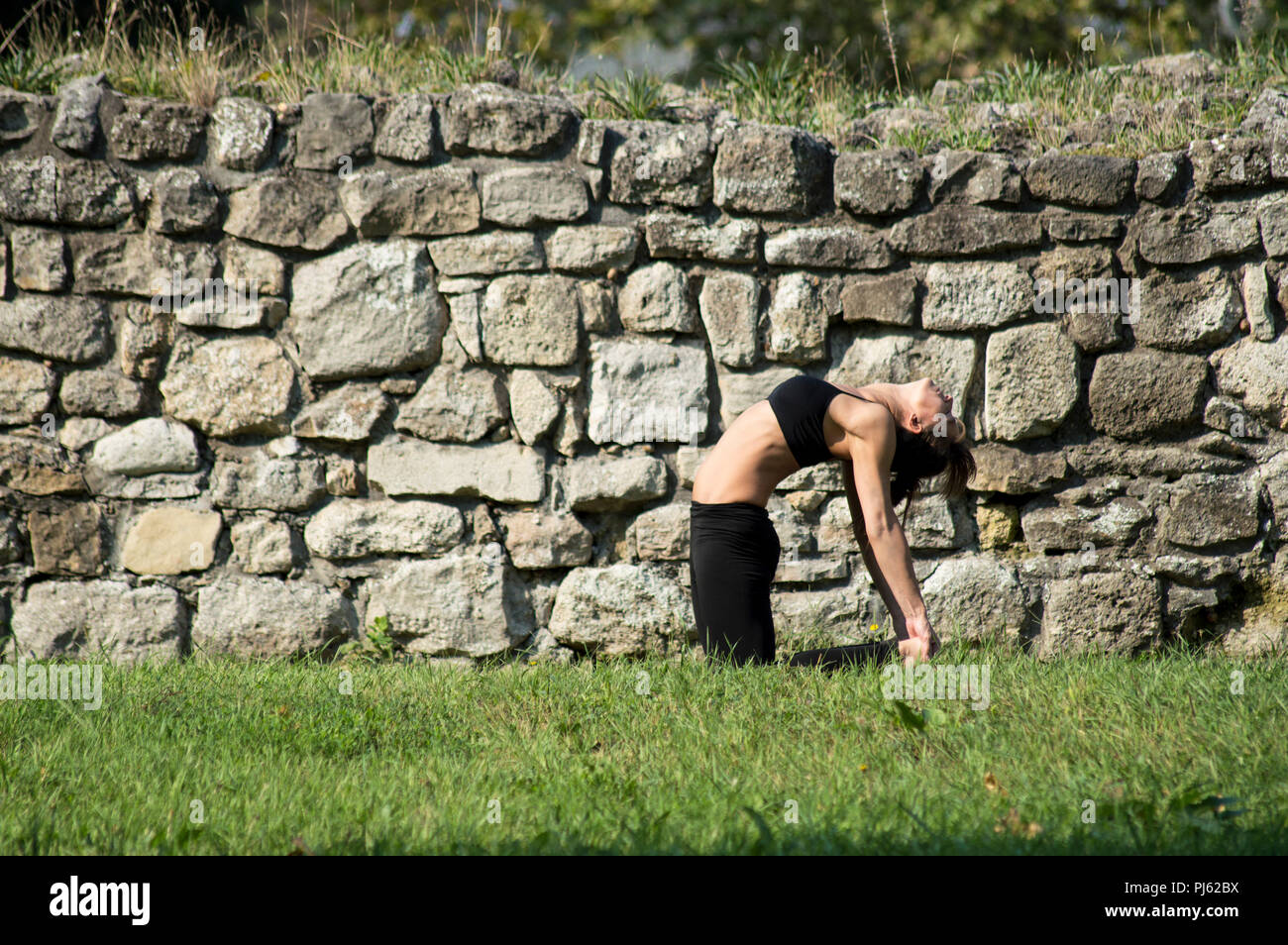 Woman practicing yoga outdoors, in Camel pose. Stock Photo