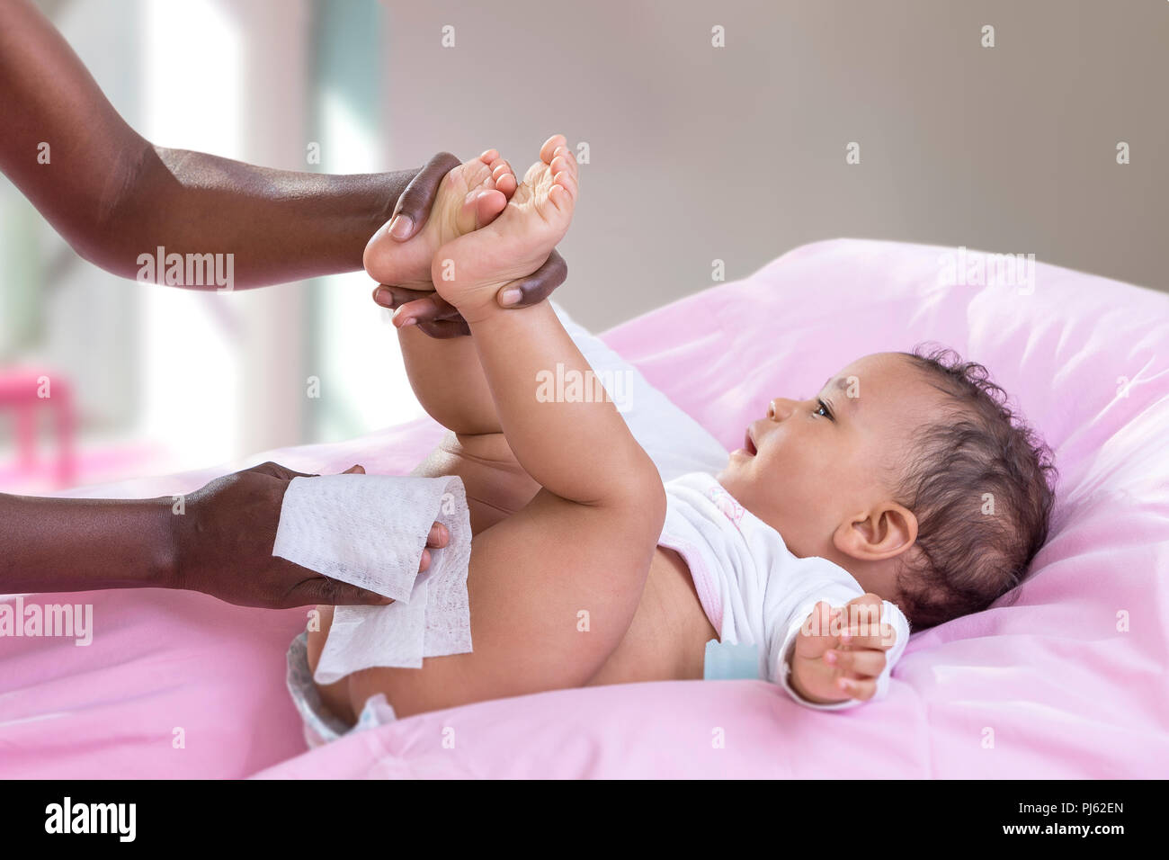 Hygiene Child. Side view portrait of a happy Afrriican, American, mother changing diaper to her baby on her bed Stock Photo