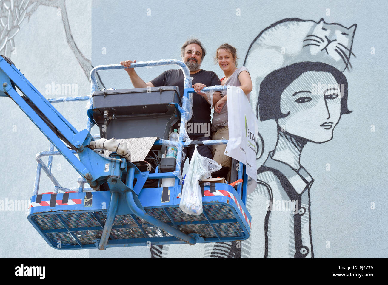 Mannheim, Germany. 23rd Aug, 2018. 23.08.2018, Baden-Württemberg, Mannheim: Christina Laube (r) and Mehrdad Zaeri from the artist duo 'Sourati' stand on a lifting platform in front of a mural sprayed onto a house wall entitled 'Abschied und Neubeginn' (lit. Farewell and New Beginning). At the end of the year, 18 huge works of art will be displayed on the facades of the North Baden city. Credit: Uwe Anspach/dpa/Alamy Live News Stock Photo