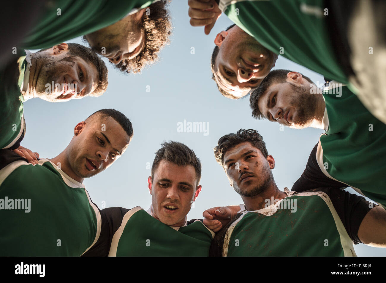Low angle view of rugby players in circle against clear sky discussing their tactics. Team of rugby player in huddle between the match. Stock Photo