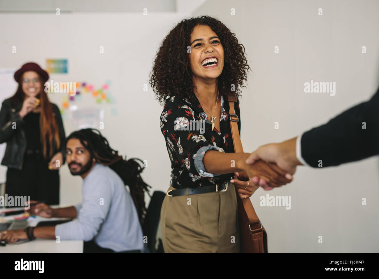 Happy business professional wearing office bag shaking hands with client. Business partners in a meeting while a businesswoman greets a customer. Stock Photo