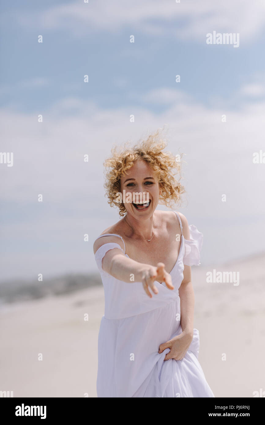 Happy woman tourist enjoying on the beach. Smiling woman in white gown running on beach reaching out for something. Stock Photo
