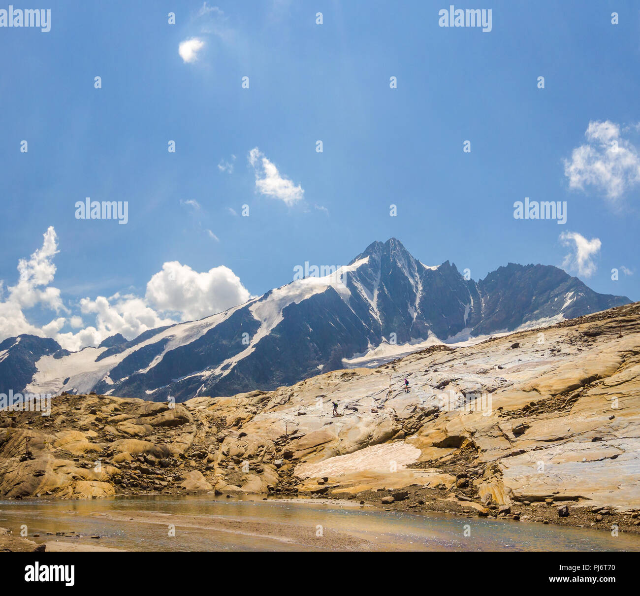 Smoothed out and round stone formation with two hikers in front of the Grossglockner Mountain in Austria Stock Photo