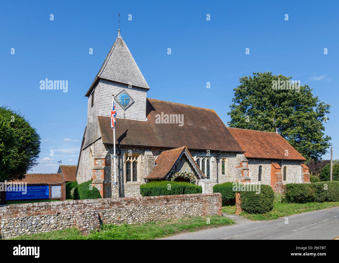 Roadside view of Church of St Thomas of Canterbury and its flint churchyard wall in East Clandon, a small village in Surrey near Guildford, SE England Stock Photo