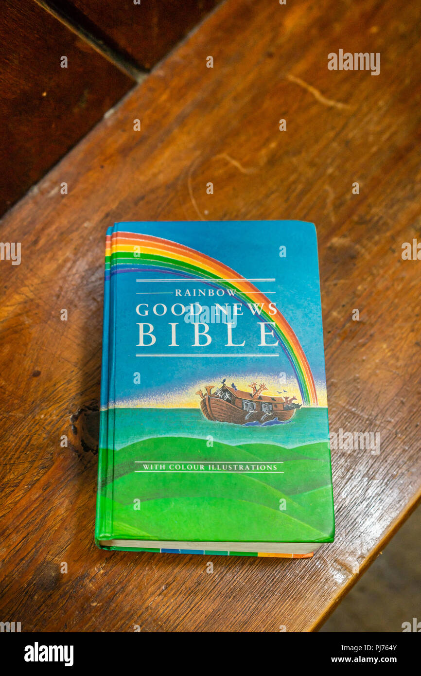 A copy of the Rainbow Good News Bible on a wooden church bank in England, UK Stock Photo