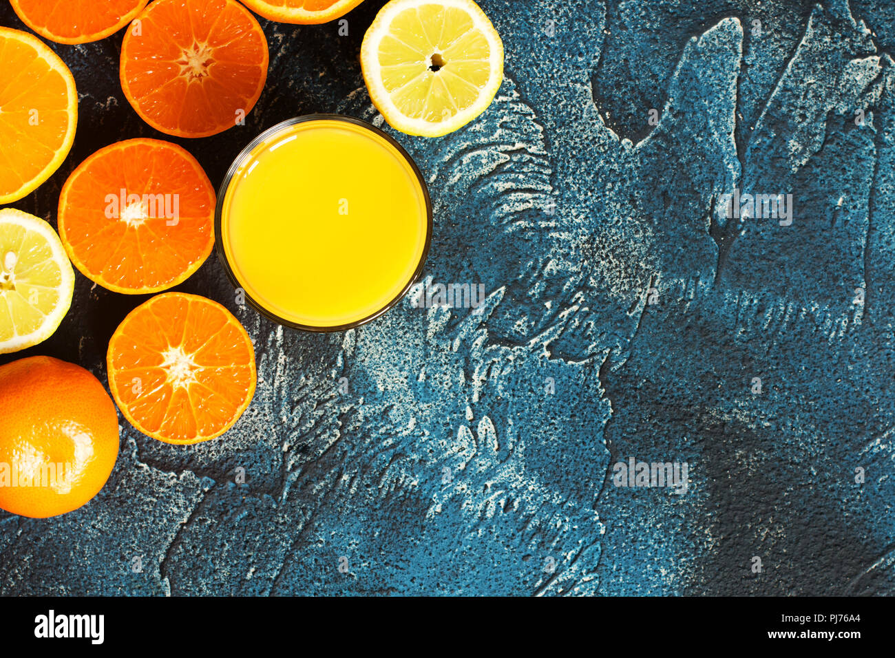 Fresh juice made of oranges, lemon, satsumas on the dark blue textured