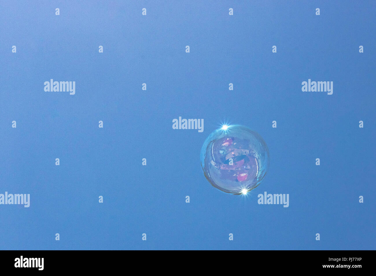 Closeup of single bubble floating in background of blue sky with reflections in bubble Stock Photo