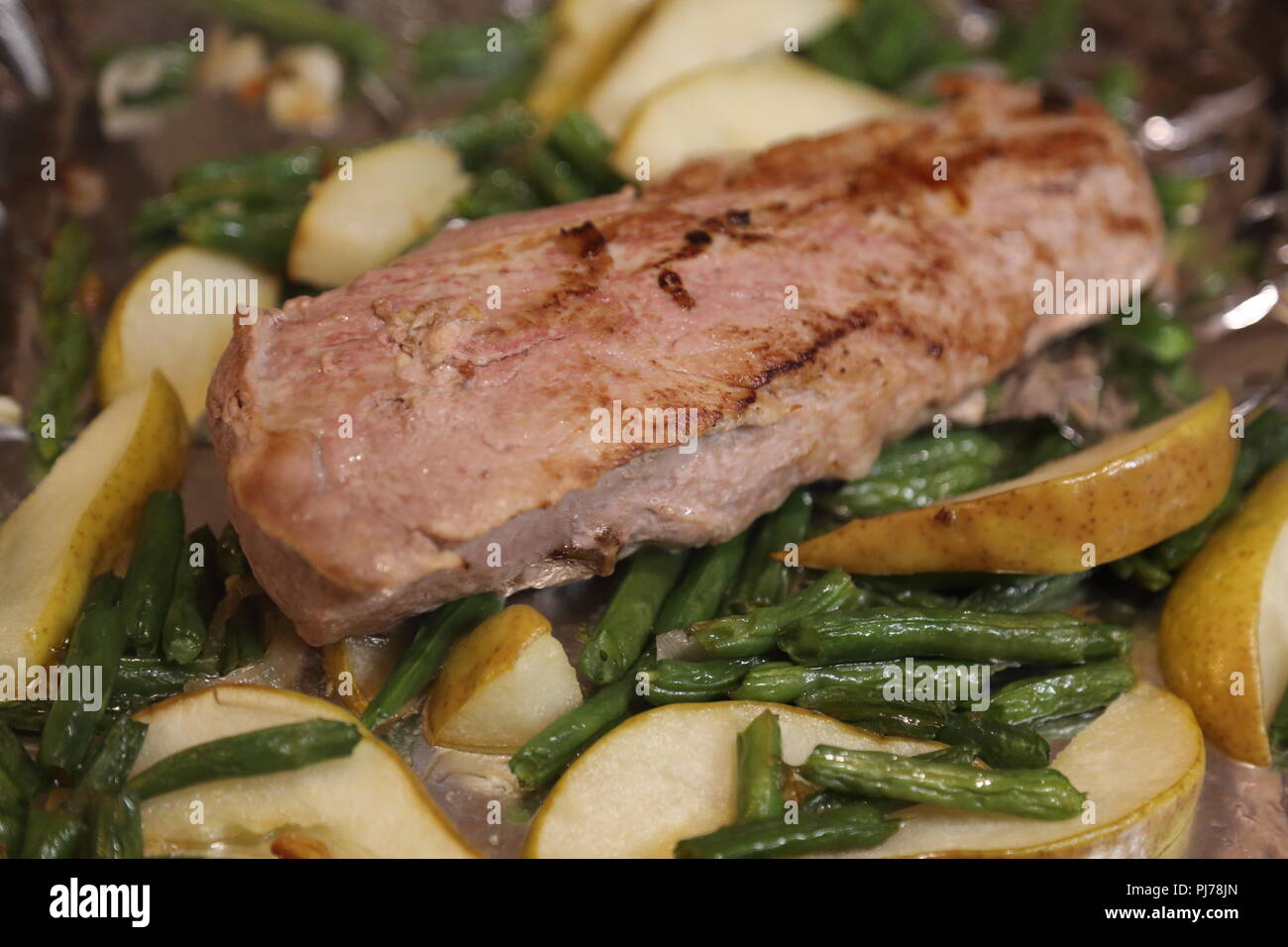 Roast port tenderloin plated with roasted pears, broccoli, and red onions Stock Photo