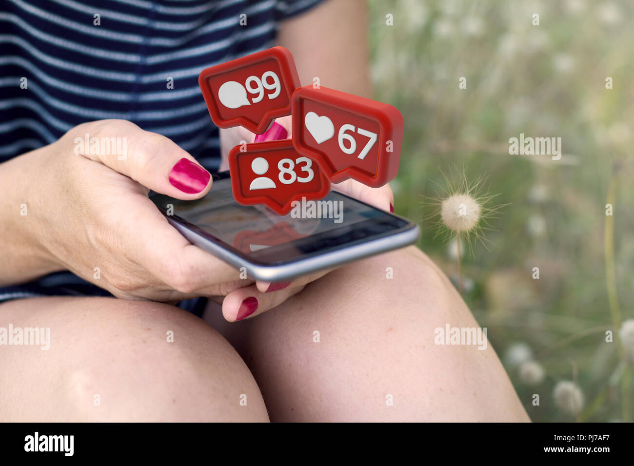 sitting woman checking notifications on smartphone on the grass. All screen graphics are made up. Stock Photo