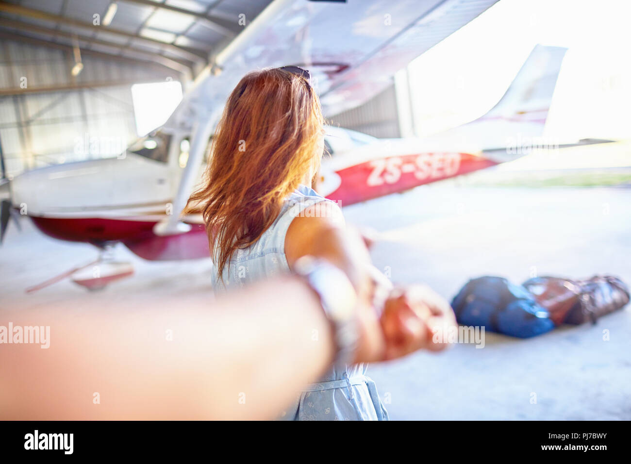 Personal perspective woman leading man by the hand toward small airplane in airplane hangar Stock Photo