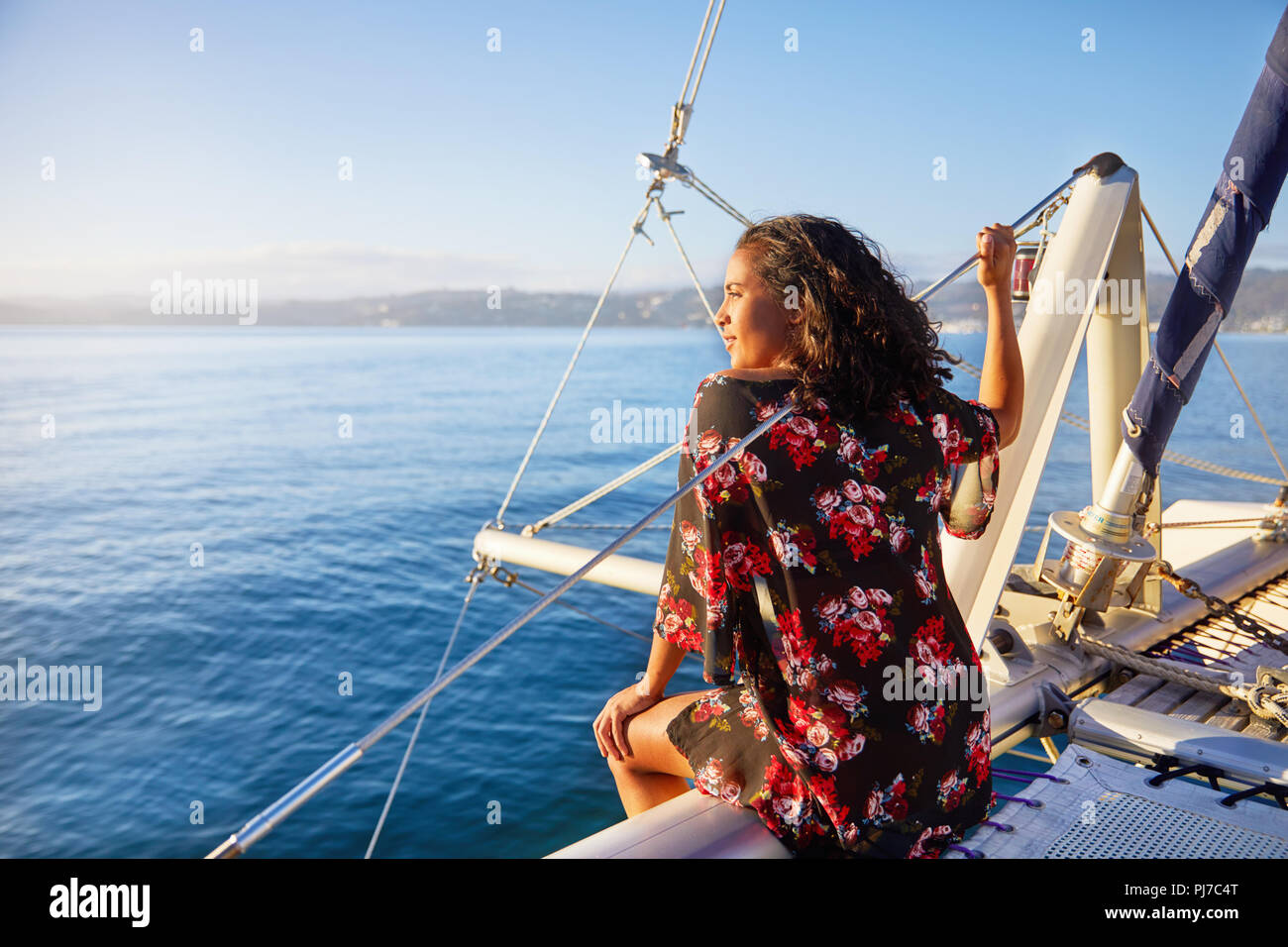 Serene young woman relaxing on sunny catamaran, looking out at blue ocean Stock Photo