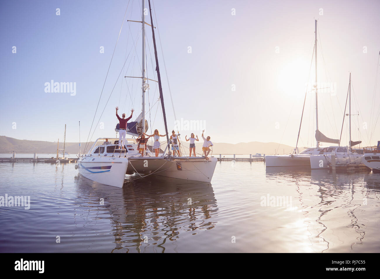 Portrait friends waving on catamaran in sunny harbor Stock Photo