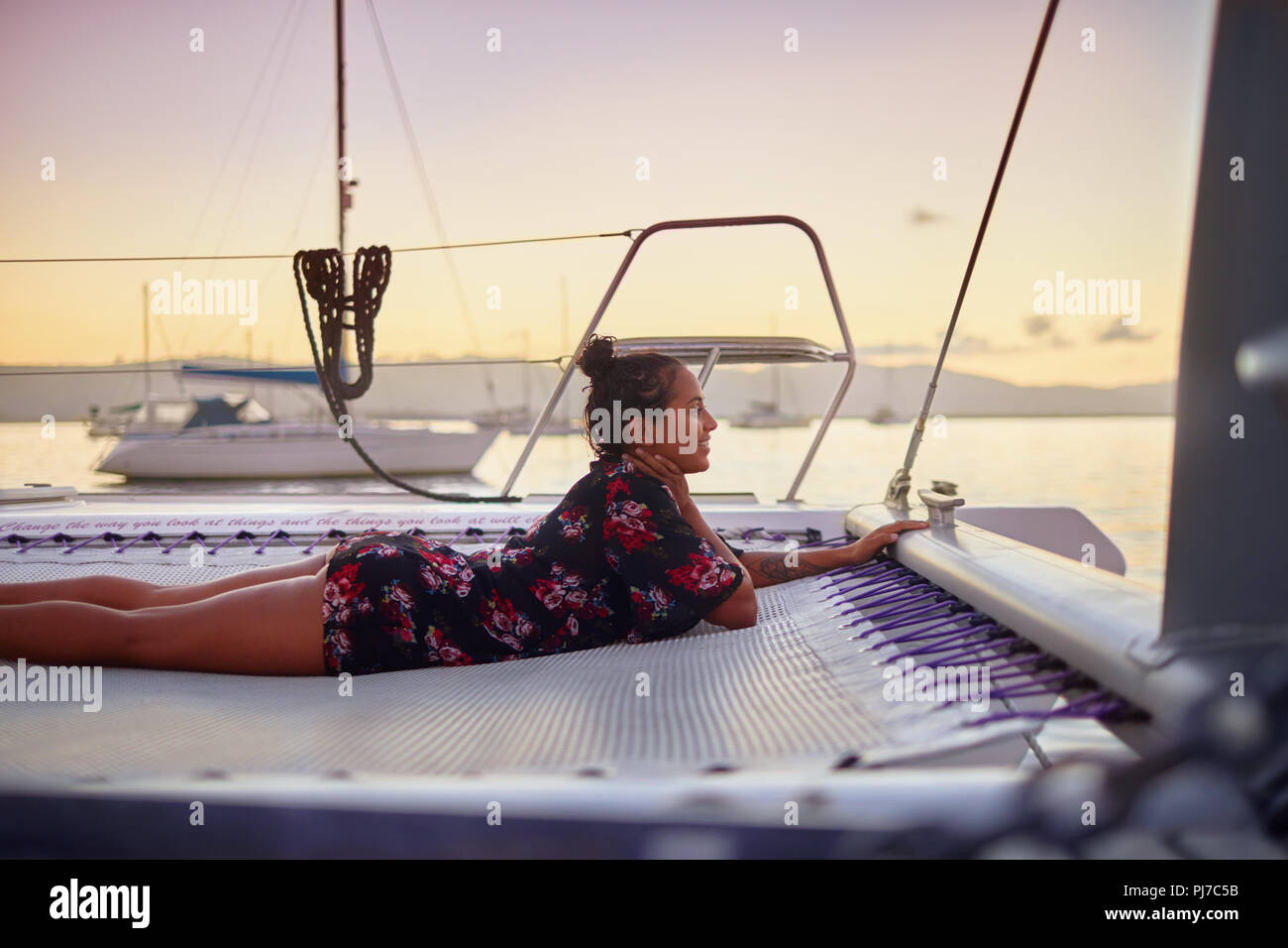 Serene young woman relaxing on catamaran net at sunset Stock Photo