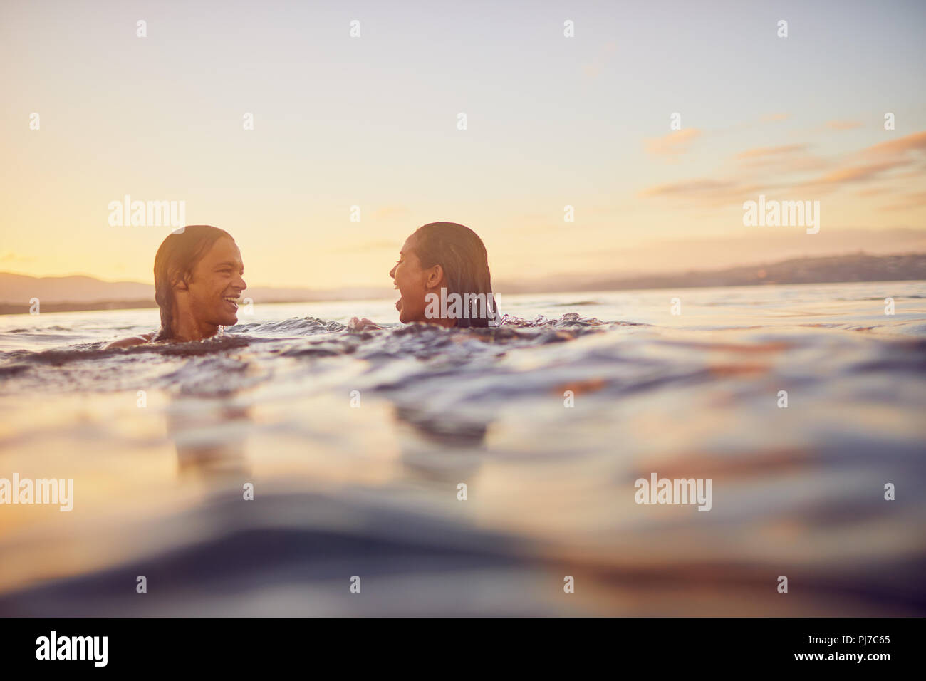 Young couple swimming in ocean at sunset Stock Photo