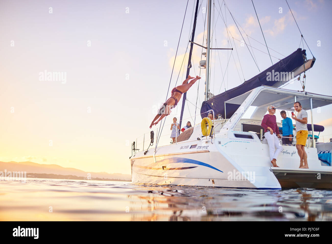 Young woman diving off catamaran into ocean Stock Photo