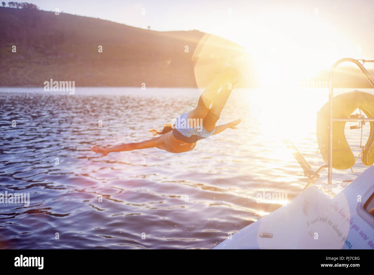 Woman jumping off boat into sunny ocean Stock Photo