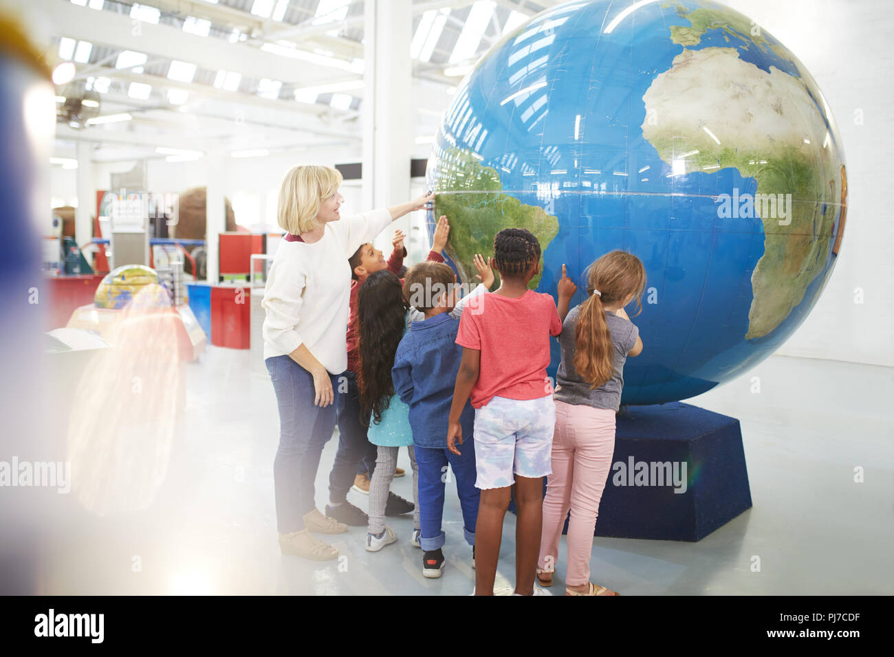 Teacher and students touching large globe in science center Stock Photo