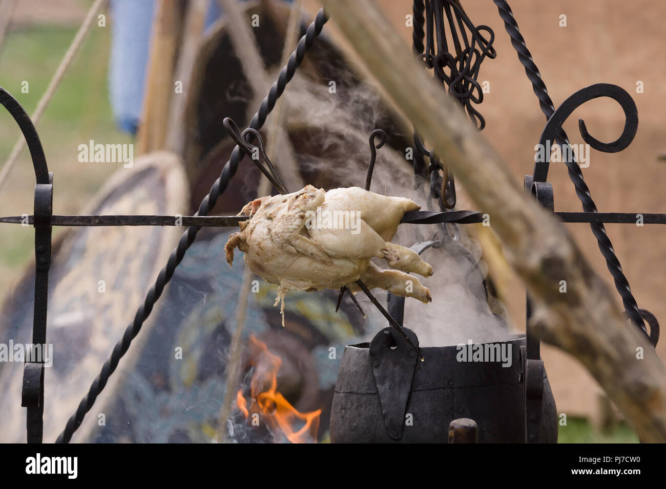 A medieval roasting spit with cauldron or cooking pot suspended on a hanger over an open fire Stock Photo