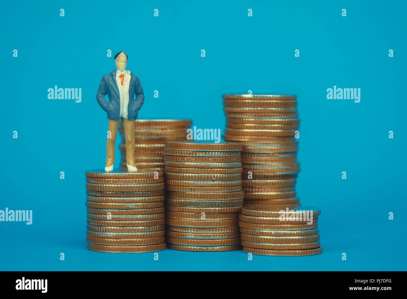 A miniature figurine man posing as a bank manager standing on some coins  with people sitting down Stock Photo - Alamy