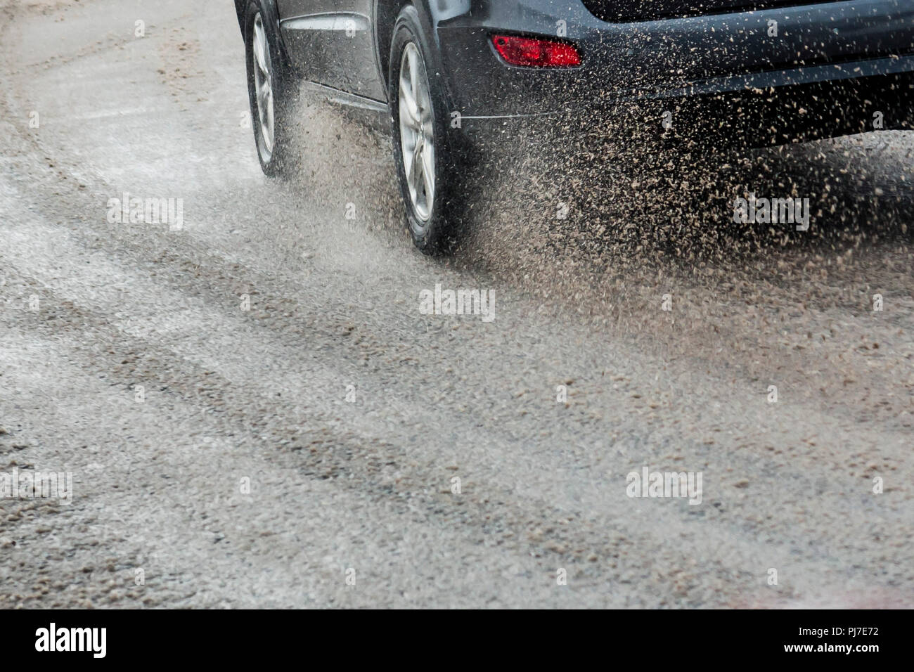 A passing car sprays an arc of icy water and slush. Stock Photo