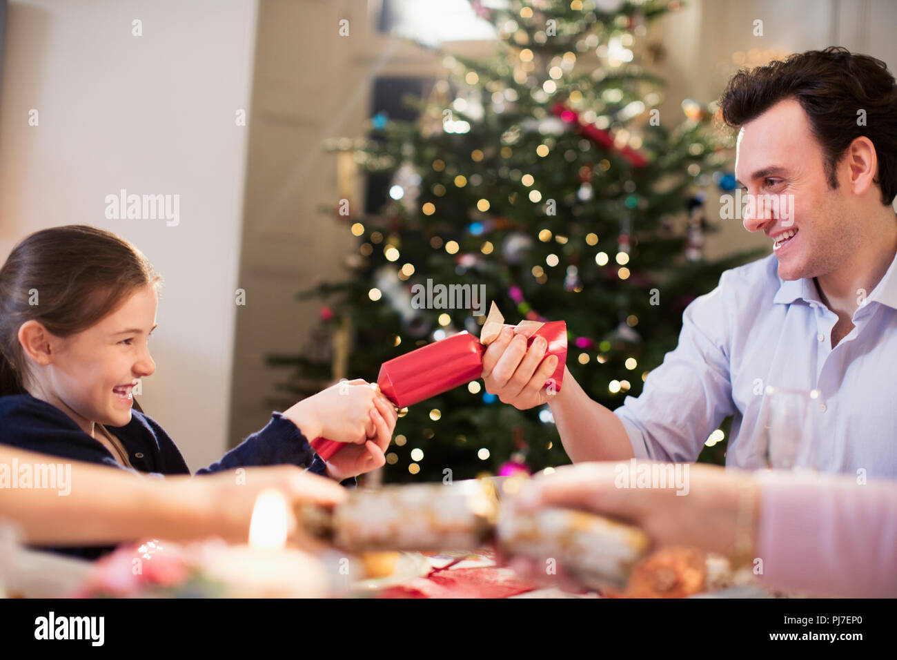 Father and daughter pulling Christmas cracker at dinner table Stock Photo