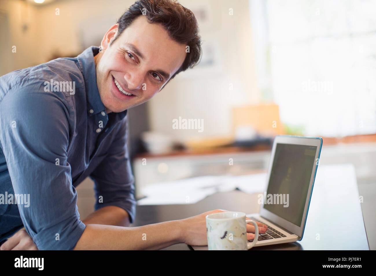 Smiling, confident man working at laptop in kitchen Stock Photo