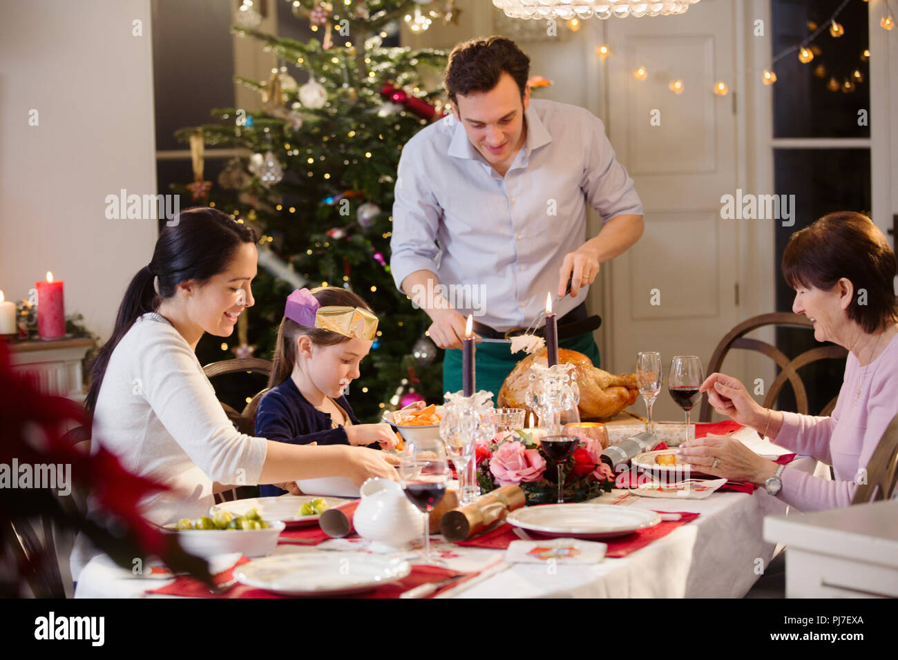 Multi-generation family carving Christmas turkey at candlelight dinner table Stock Photo