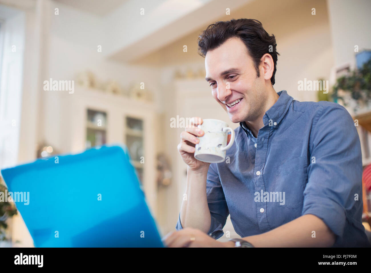 Smiling man drinking coffee, working at laptop Stock Photo