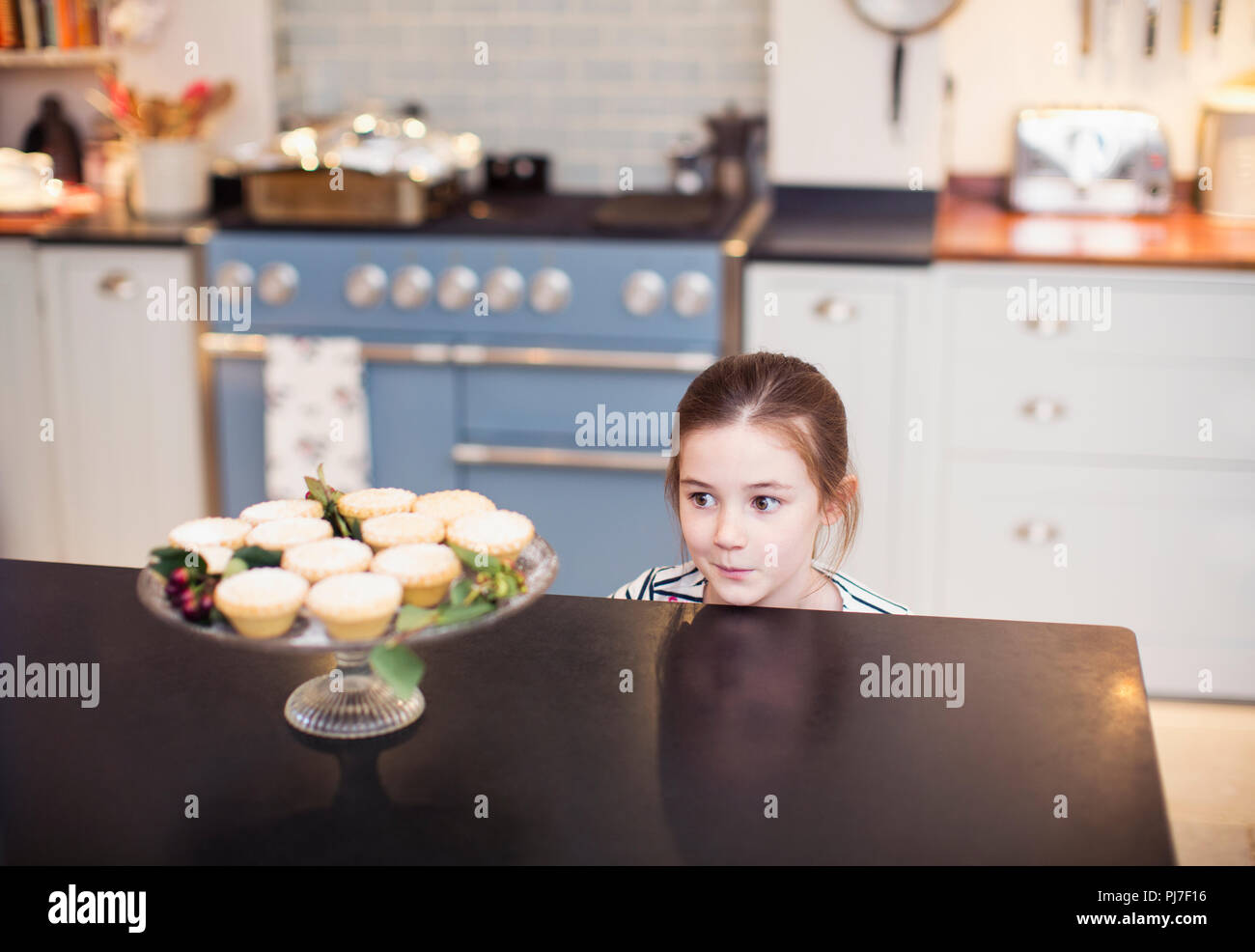 Cute girl eyeing Christmas pies on kitchen counter Stock Photo
