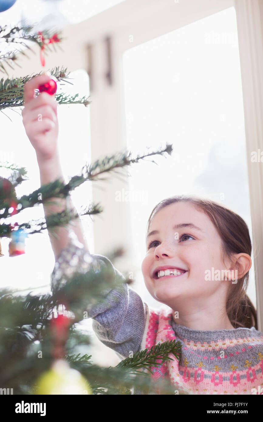 Smiling, curious girl touching ornament on Christmas tree Stock Photo