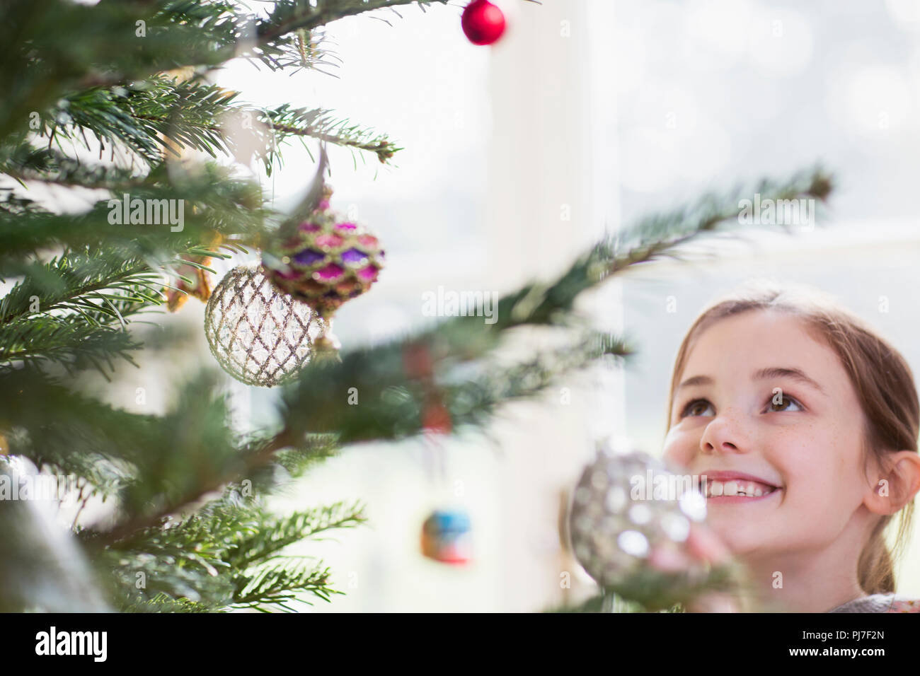 Smiling girl looking up at ornaments on Christmas tree Stock Photo