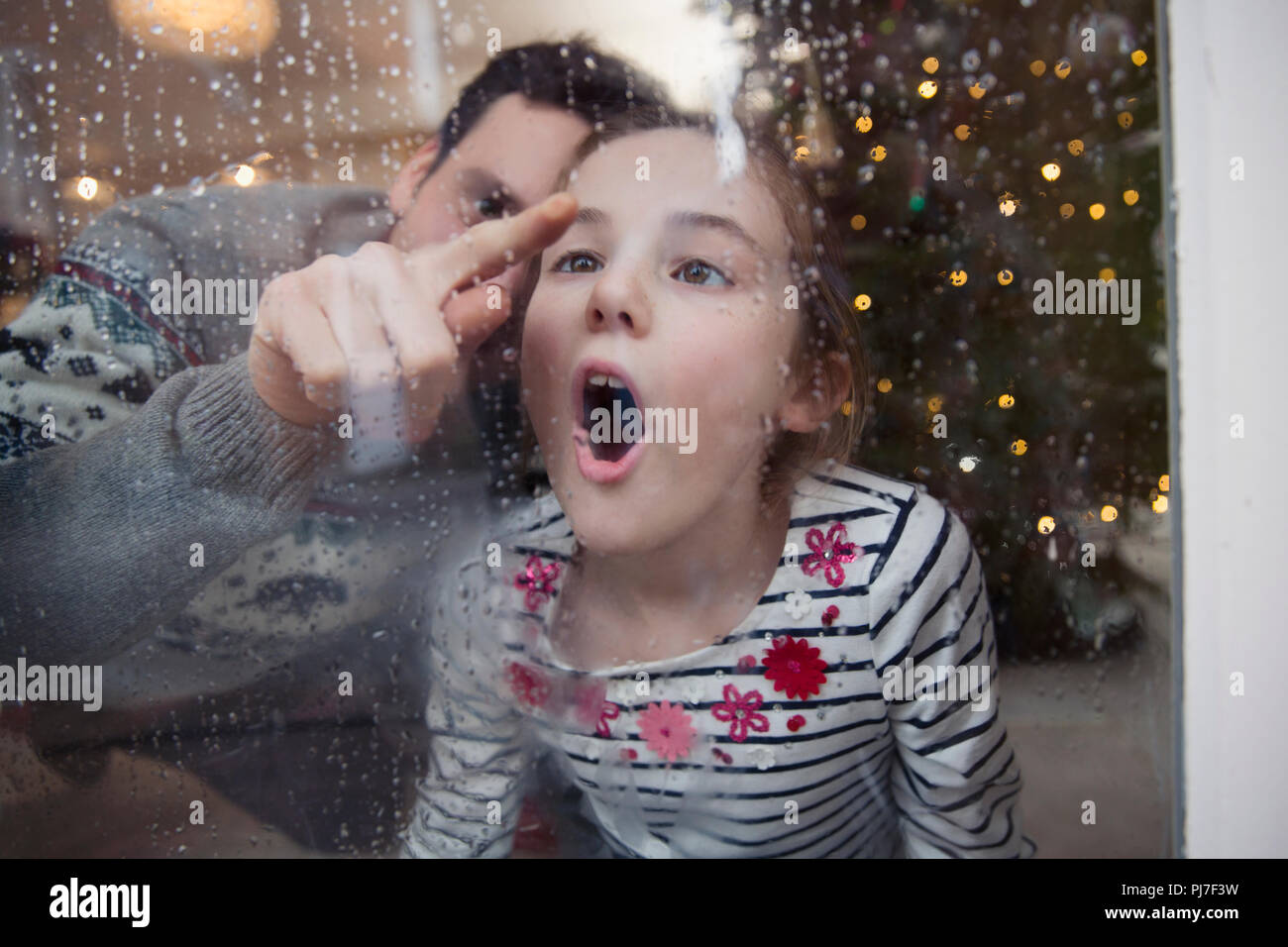 Playful father and daughter drawing in condensation on wet winter window Stock Photo