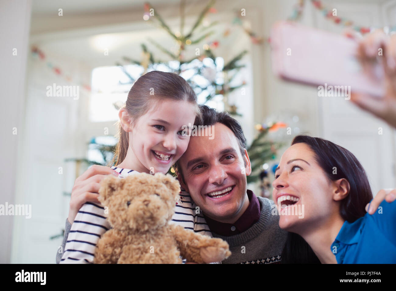 Happy parents and daughter taking selfie in front of Christmas tree Stock Photo